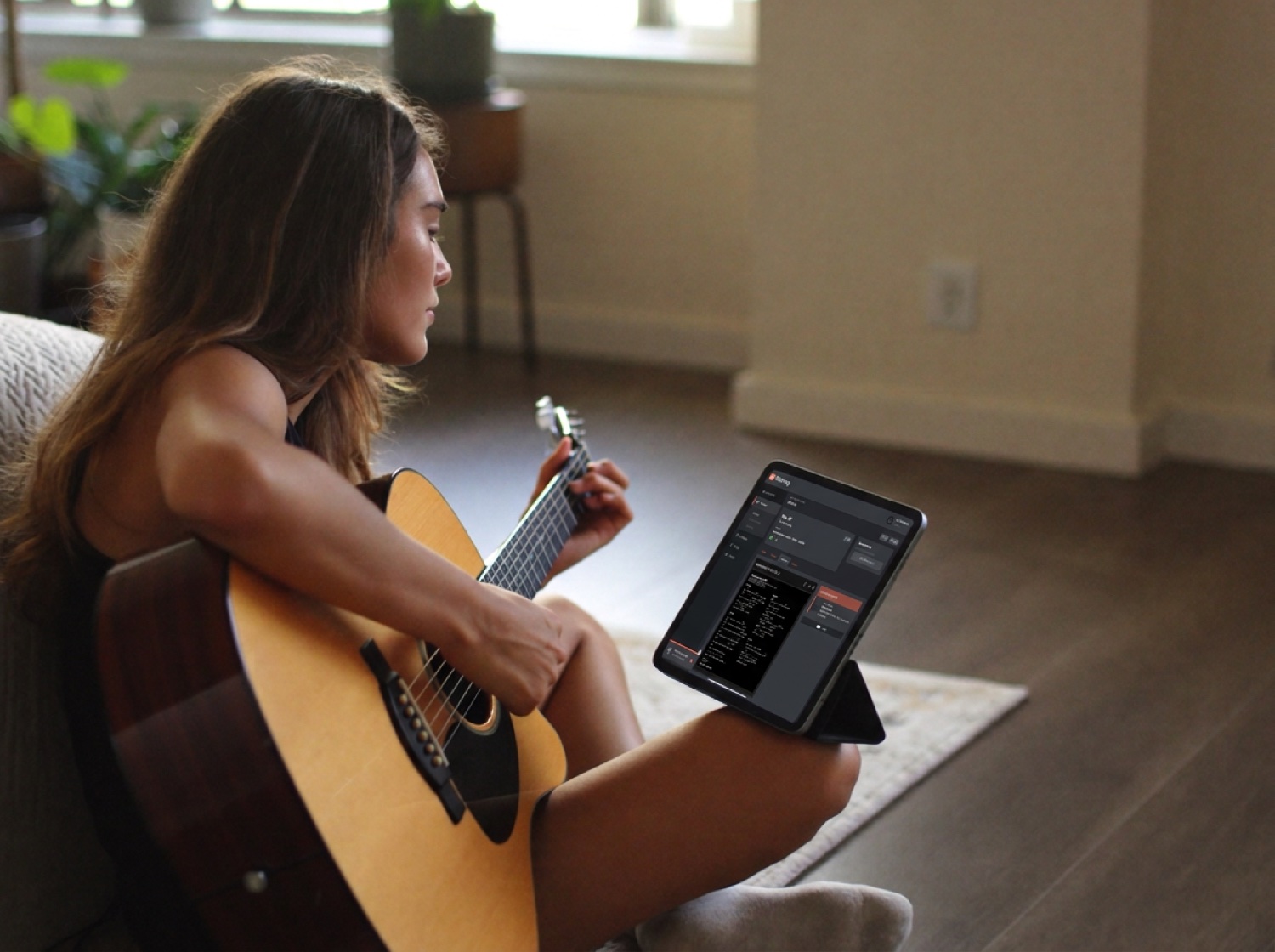 A worship musician practicing acoustic guitar at home with the Planning app open on her iPad