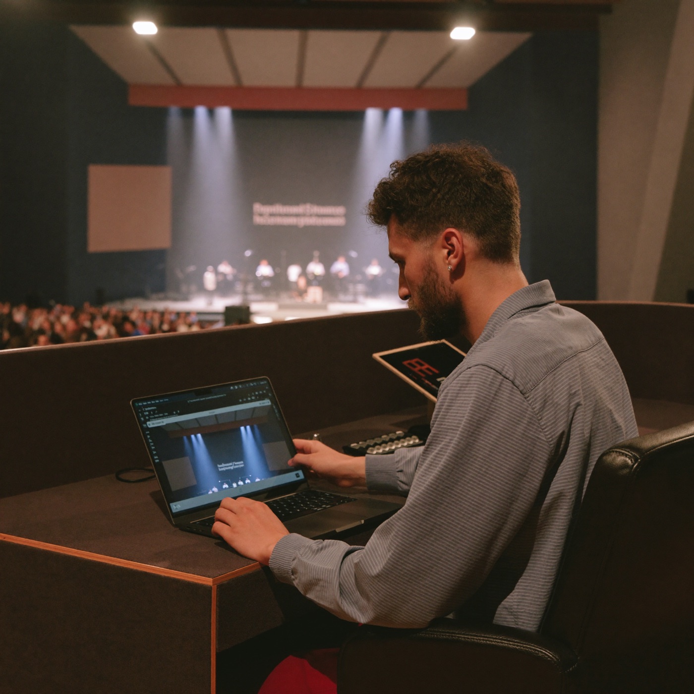 A media volunteer running the worship presentation on a laptop from the tech booth